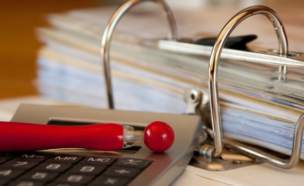 A red pen, a calculator and bills on a desk.A CPA can help you with your organization’s financial operations