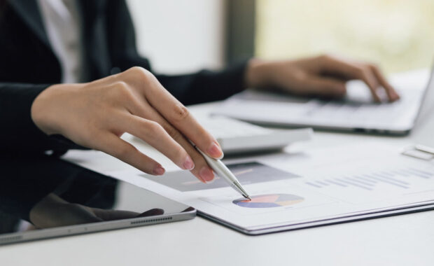 woman holding pen pointing at company sales report financial documents to analyze financial planning and growth marketing