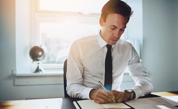 cpa reviewing contracts and taking notes in a ledger for their compliance audit