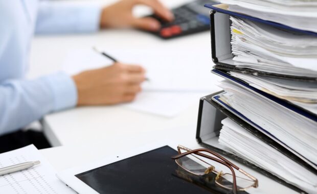 binders with papers are waiting to be processed by business woman or bookkeeper back in blur