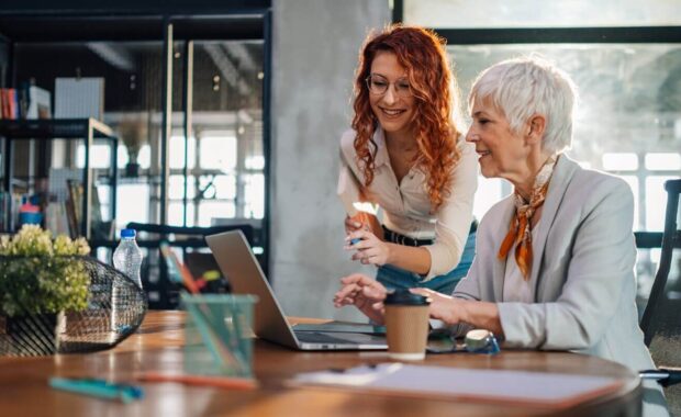 an old and young businesswomen smiling at laptop at the office