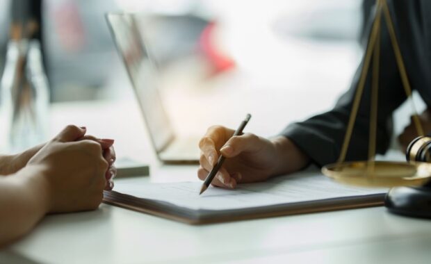 business woman and lawyers discussing contract papers with brass scale on wooden desk in office